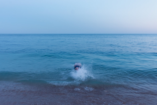 Blurred movement of the man of the sea. Abstract background of a man jumping into the water. Blue seawater on long exposure. Conceptual summer minimalism. Funny movement. Summer holidays, vacations