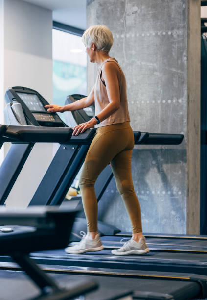 An Anonymous Senior Woman Adjusting A Treadmill Before Exercising