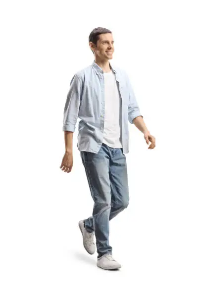 Photo of Full length shot of a happy young man in jeans and shirt walking