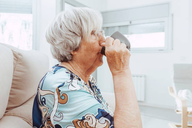 istock Elderly woman drinking coffee sitting on couch 1359985532