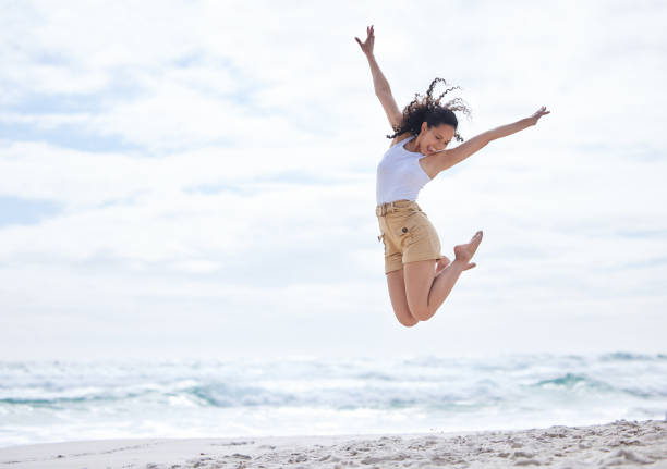 foto de una joven pasando un día en la playa - jumping freedom women beach fotografías e imágenes de stock