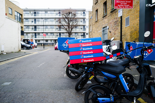 London, UK - 17 December, 2021: color image depicting a stack of Domino's Pizza boxes on the back of a delivery bike, waiting to be delivered to customers in the city.
