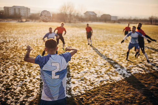 Group of people, male soccer players playing a match on a soccer field on winter day outdoors. One man is throwing in a a ball from out.