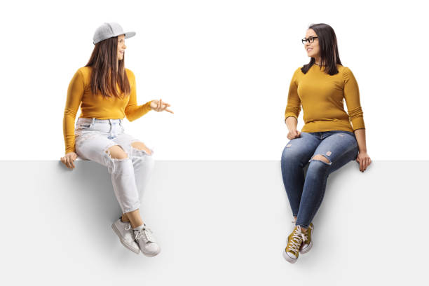 istock Two young female friends sitting on a blank panel and having a conversation 1359990046