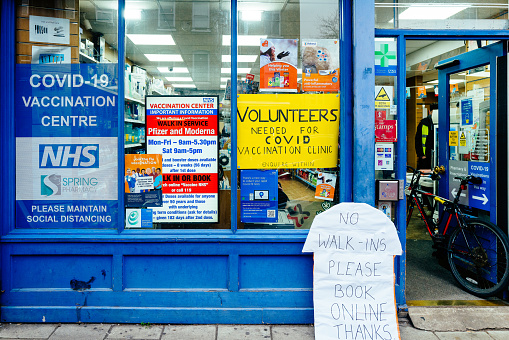 London, UK - 17 December, 2021: exterior of a Covid-19 vaccination clinic on a city street in London, UK. The window is covered with signs, including one calling for volunteers to help with vaccinations.