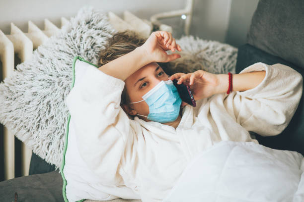 istock Sick woman with face protective mask using mobile phone and lying in bed 1359992271