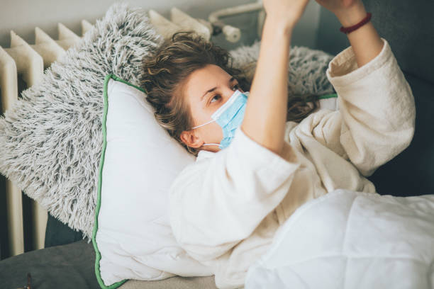 istock Sick woman with face protective mask using mobile phone and lying in bed 1359992478