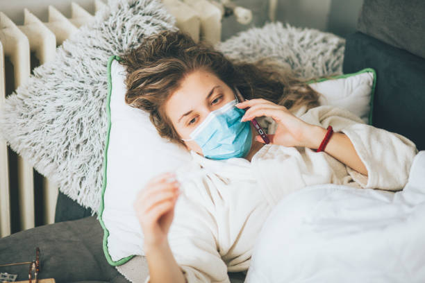 istock Sick woman with face protective mask using mobile phone and lying in bed 1359993338