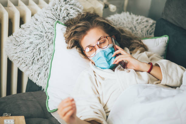 istock Sick woman with face protective mask using mobile phone and lying in bed 1359993397