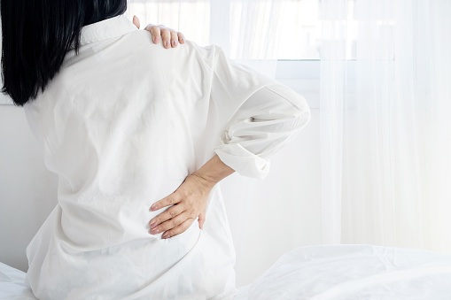 woman suffering from neck, shoulder and lower back pain sitting in bed wakeup in the morning feeling pain muscles and nerve