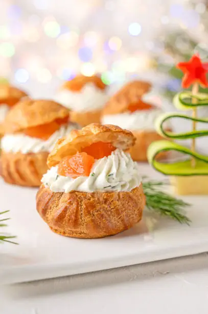 Festive savory profiteroles with salmon, cream cheese and dill on a white plate on a white background. Appetizer for Christmas and New Year. Selective focus