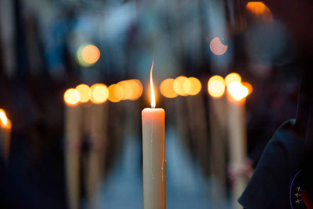 selektywne skupienie szczegółu zapalonej świecy niesionej przez penitenta, podczas procesji wielkiego tygodnia w hiszpanii, z nieostrymi światłami osób następnych w kolejce - christianity spirituality religion one way zdjęcia i obrazy z banku zdjęć