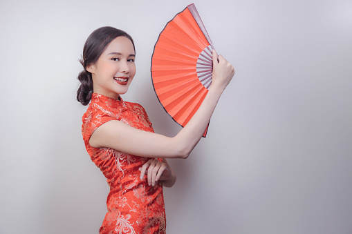 Asian woman in national dress of Chinese new year holding red  wood fan and smiled in soft isolated background, celebrated in attractive culture of China