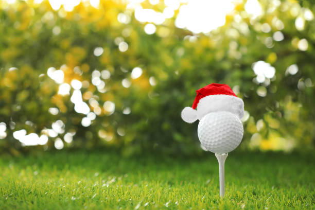 istock Golf ball with small Santa hat on tee against blurred background. Space for text 1359996485
