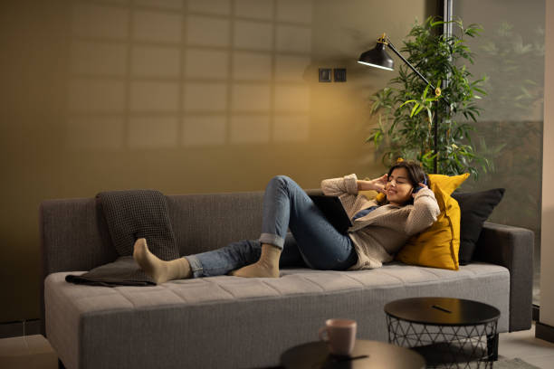 istock Young woman lying on sofa and listening music on headphones 1359996708