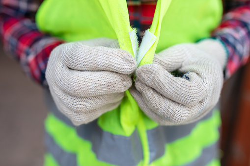 Close-up of a construction worker with hand gloves wearing reflective vest at site. Worker wearing protective workwear at site.