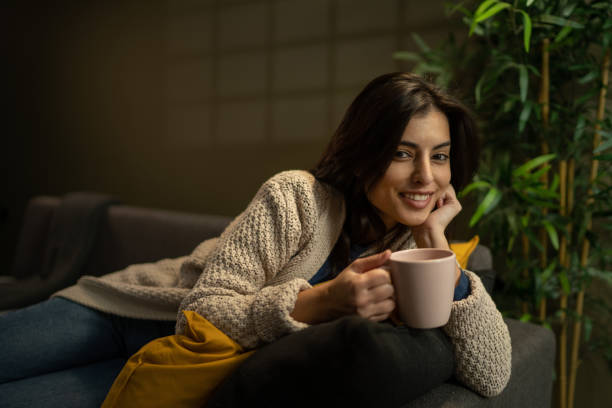 istock Smiling woman lying on sofa with tea cup and looking at camera 1360001364