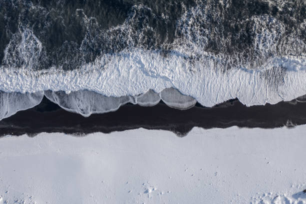 Bird's Eye View of the Black Sand Beach With Snow in Iceland The Black Sand Beach of Iceland is popular with tourists as the volcanic rock eroded by the sea turns the beach black contrasting with the ocean and snow black sand stock pictures, royalty-free photos & images