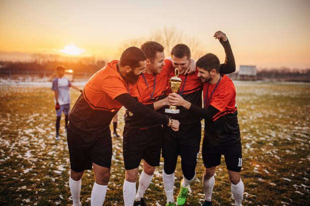 Football team celebrating a trophy Group of people, male soccer players celebrating because they won a trophy, on a soccer field on winter day outdoors. soccer team captain stock pictures, royalty-free photos & images