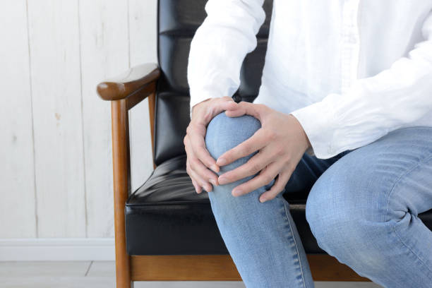 Woman holding painful knee in living room Woman holding painful knee in living room hugging knees stock pictures, royalty-free photos & images