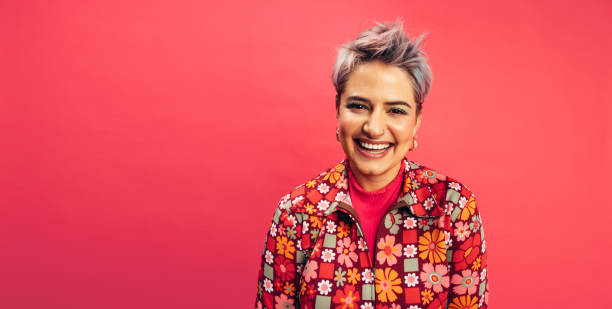 Hipster woman smiling at the camera Hipster woman looking at the camera with a happy smile on her face. Cheerful young woman standing alone against a red background. Fashionable young woman with dyed hair feeling vibrant. pink hair stock pictures, royalty-free photos & images