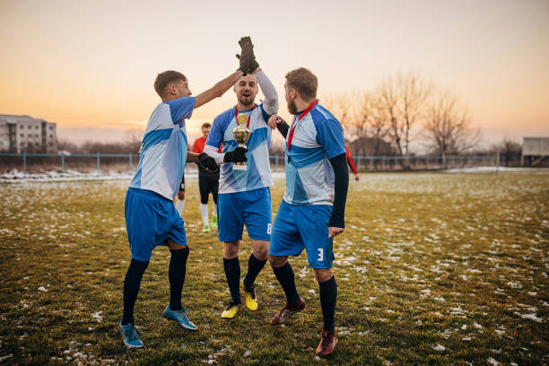 Group of people, male soccer players celebrating because they won a trophy, on a soccer field on winter day outdoors.