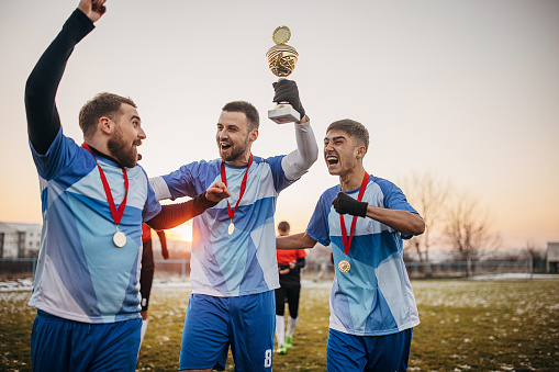 Group of people, male soccer players celebrating because they won a trophy, on a soccer field on winter day outdoors.