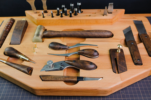 Exclusive handmade leather craft tools. Close up of different tanner tools on wooden box. Set of Different knifes from steel and wood. Black background.