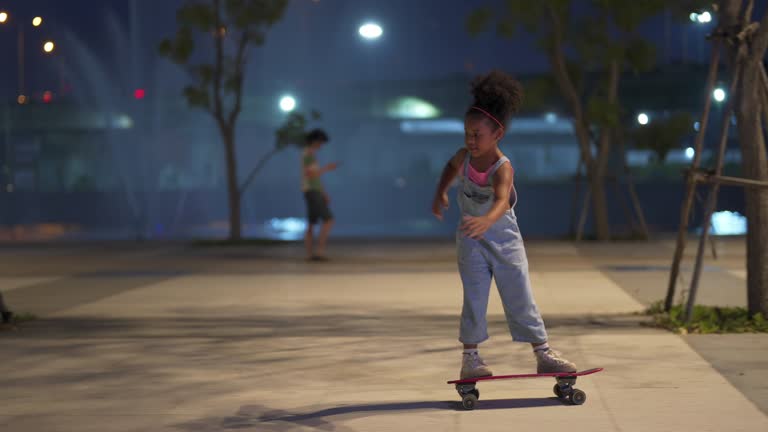 4K Little African girl skateboarding at the park on summer vacation night.