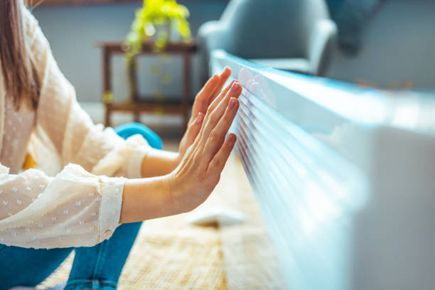 Cold home, freezing. Cold home, freezing. Using heater at home in winter. Woman warming her hands sitting by device and wearing warm clothes. Heating season. Woman warms up hands over heater. heat home interior comfortable human foot stock pictures, royalty-free photos & images