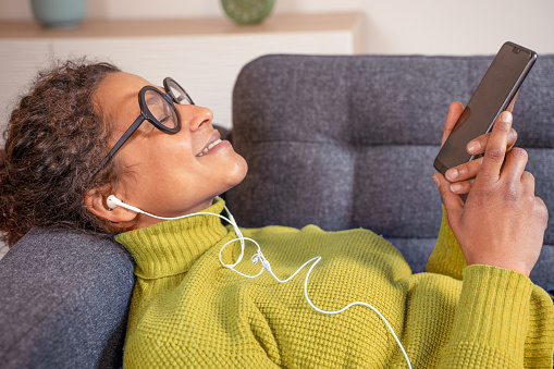 Black woman relaxing and listening to music holding phone
