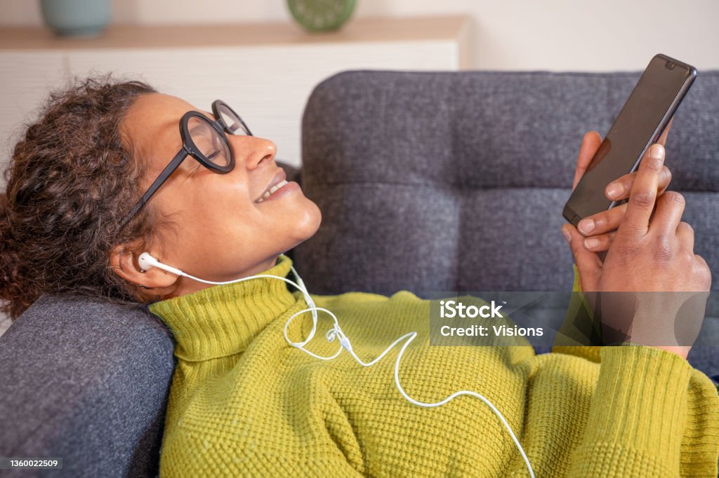 Black woman relaxing and listening to music holding phone Cheerful black woman listening to music using smartphone Music Streaming Service Stock Photo
