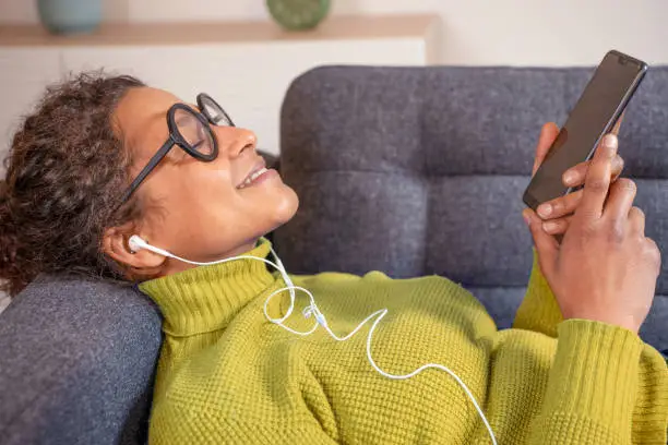 Photo of Black woman relaxing and listening to music holding phone