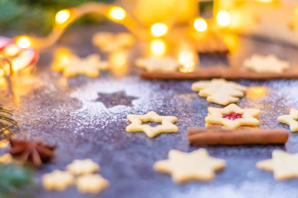 istock Christmas sweets and cookies placed on gray desk. Winter decorations, pine tree and cone. Concept of christmas, gifts and holidays. Glowing lights in the background. 1360023778