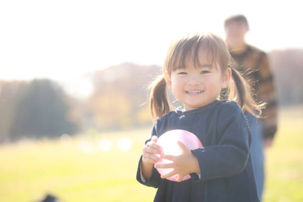 A portrait of a small toddler girl holding balloon in park in sunny autumn nature.