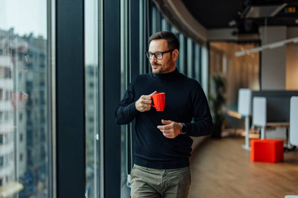 istock Serious caucasian man with glasses, gazing through the window and drinking coffe. 1360023928
