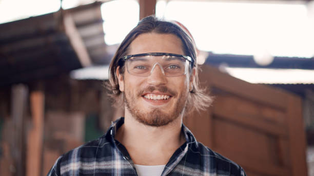 Portrait of male carpenter looking at camera Portrait of Caucasian male carpenter wearing protective glasses looking smile at camera. happy craftsman at the workshop studio protective eyewear stock pictures, royalty-free photos & images