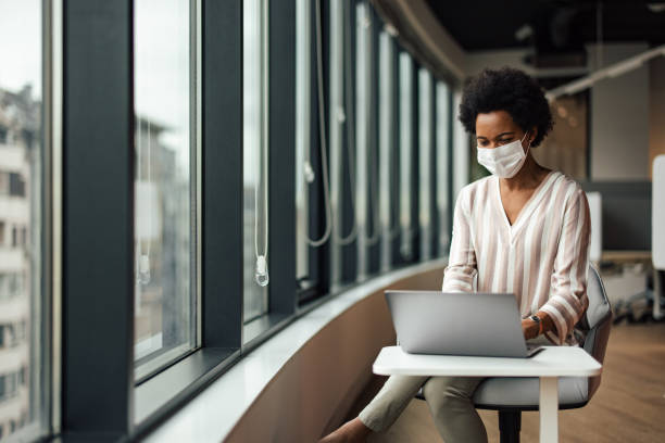 istock Thoughtful businesswoman with a mask, searching for a new solution on her laptop. 1360028113