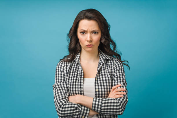 retrato de uma jovem irritada em pé sobre fundo azul isolado. olhando para a câmera - irritação - fotografias e filmes do acervo