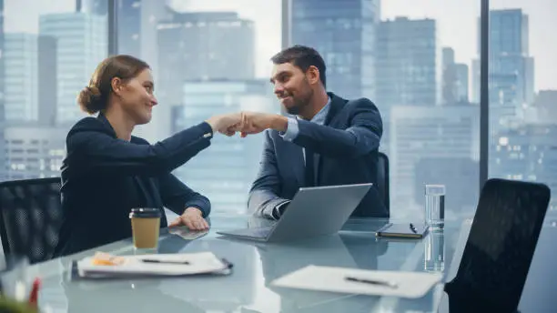 Photo of Corporate CEO and Investment Manager Talking, Using Laptop Computer while Sitting in Meeting Room in Office. Two Successful Businesspeople Fist Bump Over a Lucrative Real Estate Investment Deal.