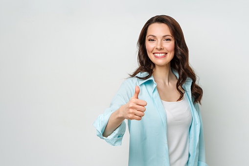 Attractive young woman , brunette, with a beaming smile, giving a thumb up gesture of approval and success
