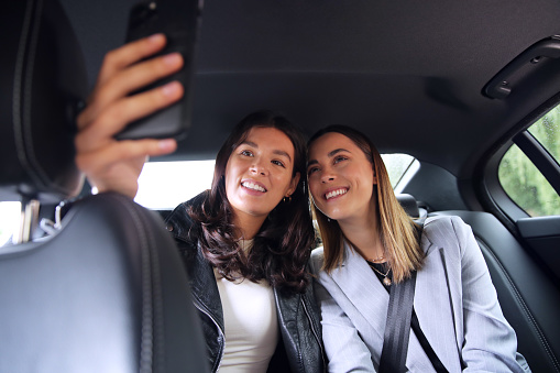 Businesswomen Commuting To Work In Back Of Car Or Taxi Taking Selfie On Mobile Phone