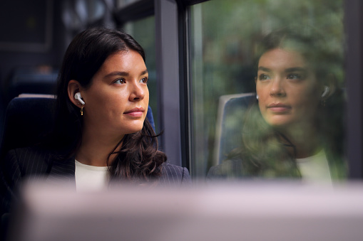 Businesswoman With Wireless Earbuds Commuting To Work On Train Looking Out Of Window
