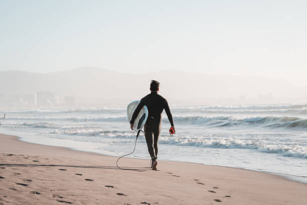surfista caminando en la playa con una tabla de surf metiéndose en el océano en la serena, chile - región de coquimbo fotografías e imágenes de stock