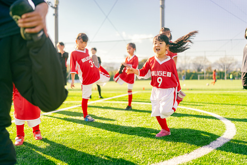 Members of female kids' soccer or football team are warming up before starting training.