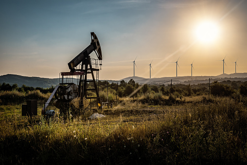 industrial oil pump and windmills on sunset