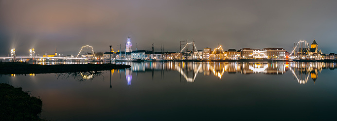 Evening on the skyline of the city of Kampen in Overijssel, The Netherlands. The lights of the city are reflected in the calm water during this cold winter night.