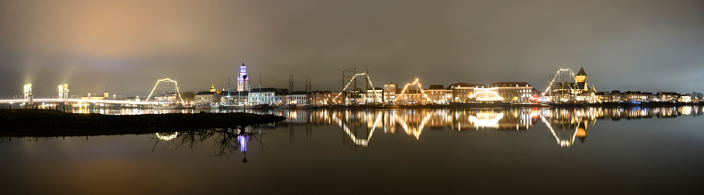 Evening on the skyline of the city of Kampen in Overijssel, The Netherlands. The lights of the city are reflected in the calm water during this cold winter night.