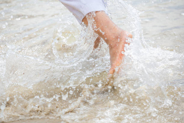 Close up woman bare feet running on the beach with sea water splashing.