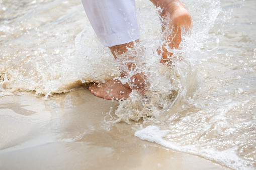 Close up woman bare feet running on the beach with sea water splashing.